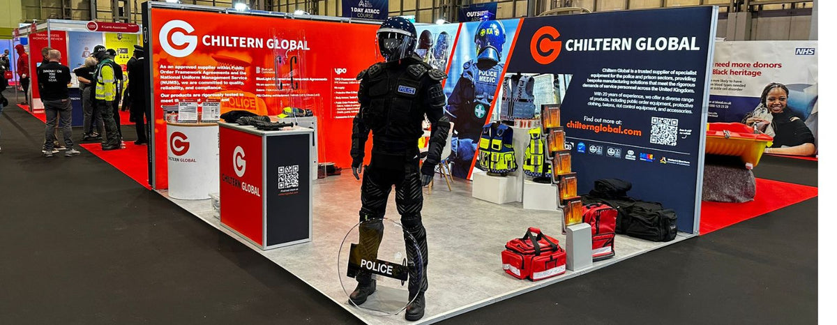 Os nossos mercados - Stand da Chiltern Global numa feira comercial com um agente de ordem pública e vários produtos em exposição.