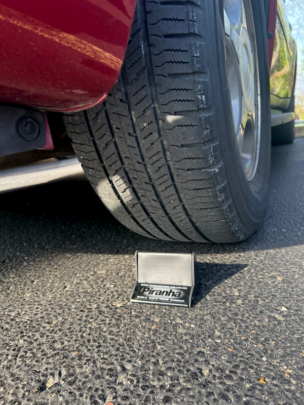 Piranha by Stop Stick in use, under a tire of a red car on a road