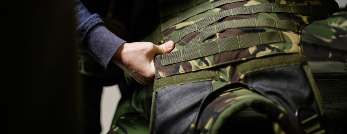 Fabrico - Pessoa a segurar um colete balístico camuflado, com destaque para o design do colete.